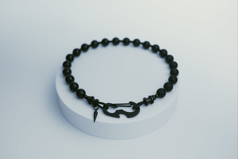 Black beaded necklace on a white pedestal with a light gray background