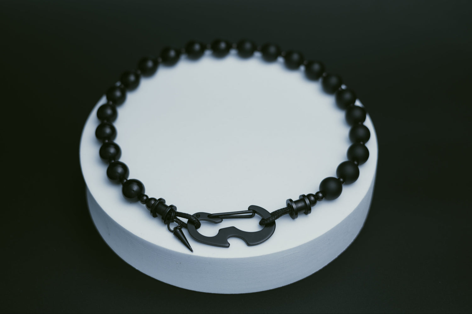 Black beaded necklace on a white circular stand against a dark background